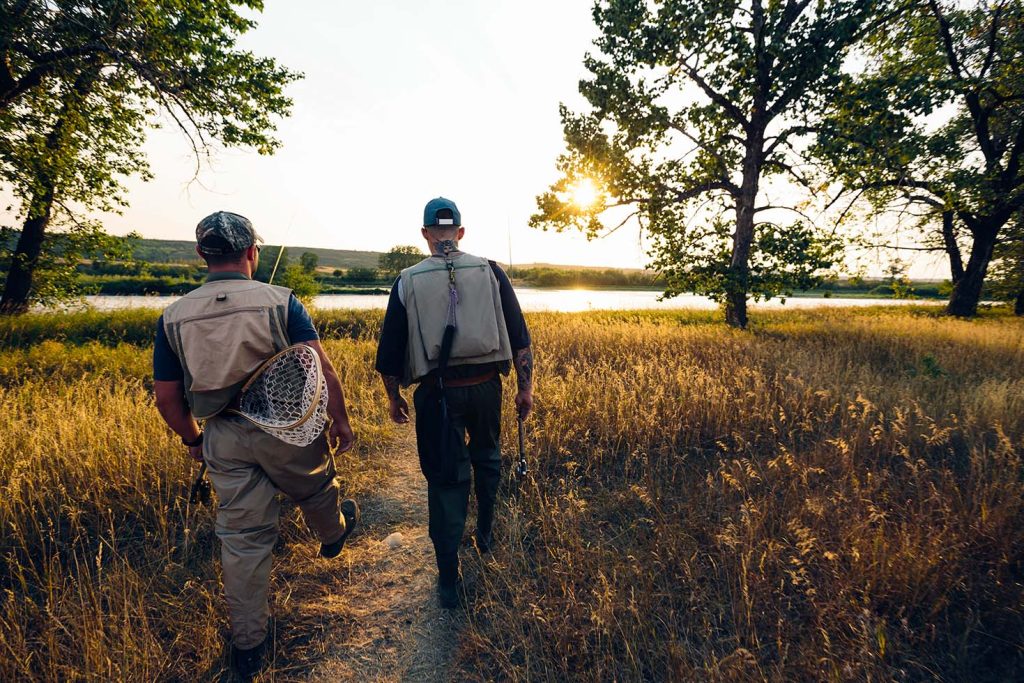 Two men with fishing rods walking towards the Bow River in Cranston as the sun rises.