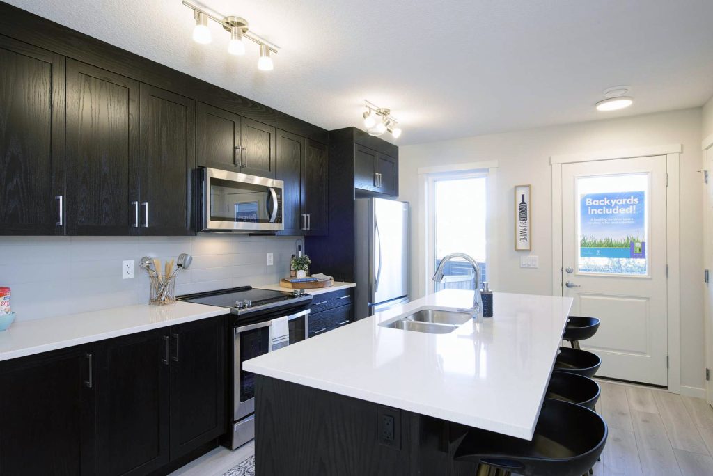 Modern ZEN Sequel Ambrosia kitchen by Avalon Homes featuring dark cabinetry, quartz island, and stainless steel appliances.