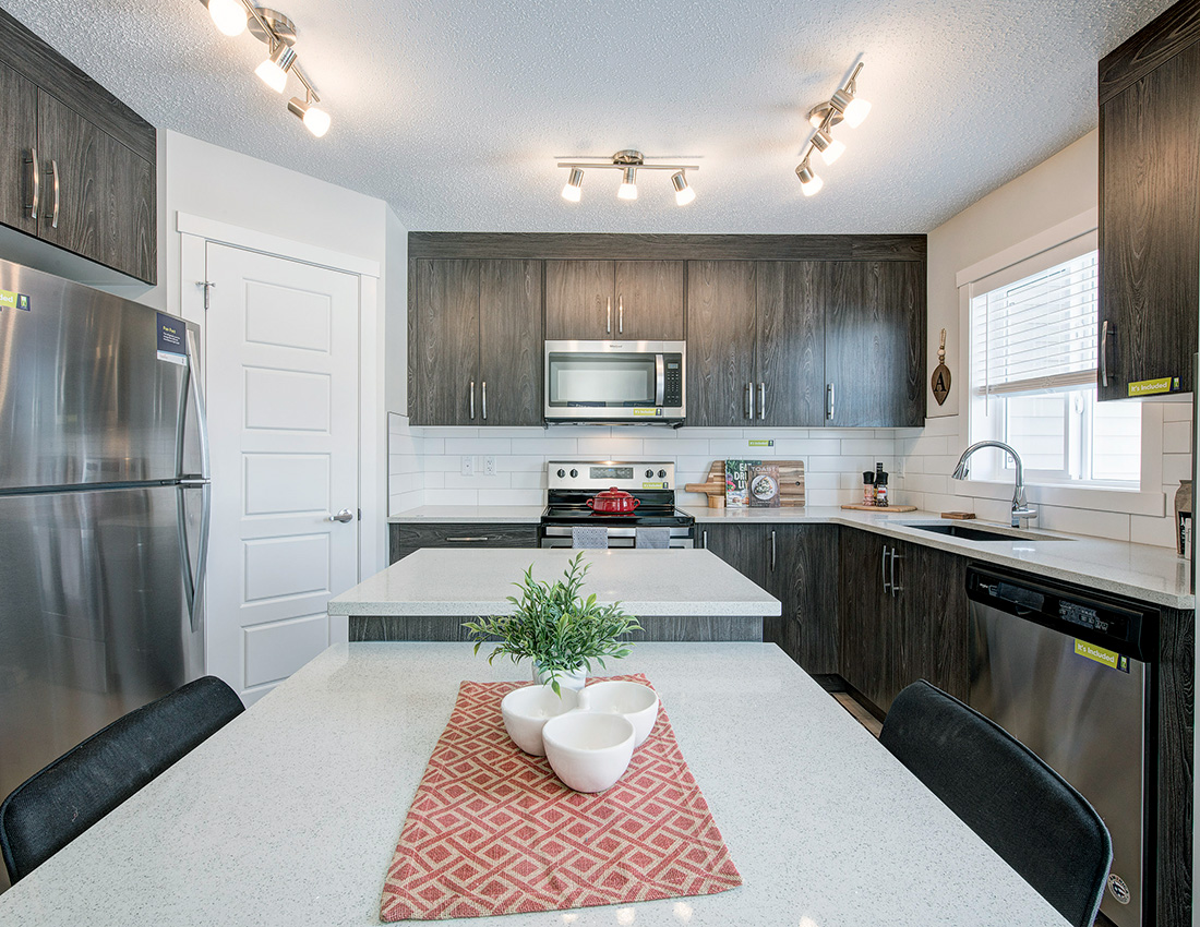 kitchen with brown cabinets, white quartz countertops, stainless steel dishwasher and fridge. A centre istland in the middle