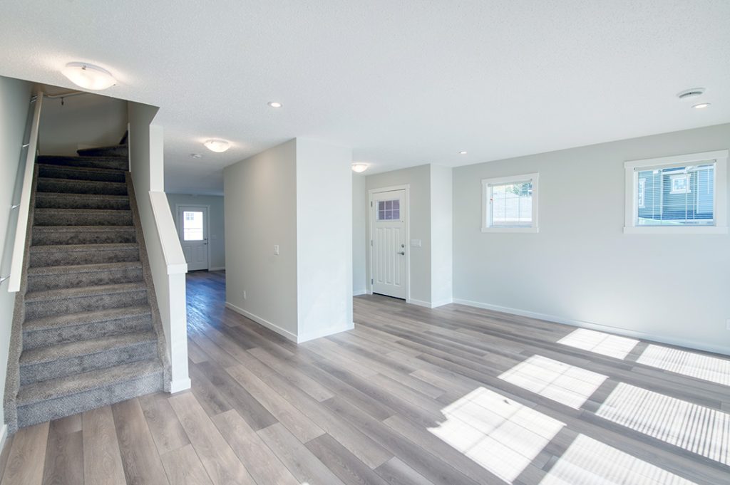 Bright townhouse entryway with wood-style flooring, carpeted stairs, and white walls with multiple windows.