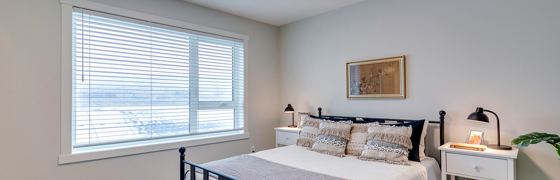 Cozy modern bedroom with large window, neutral decor, and soft lighting from bedside lamps.
