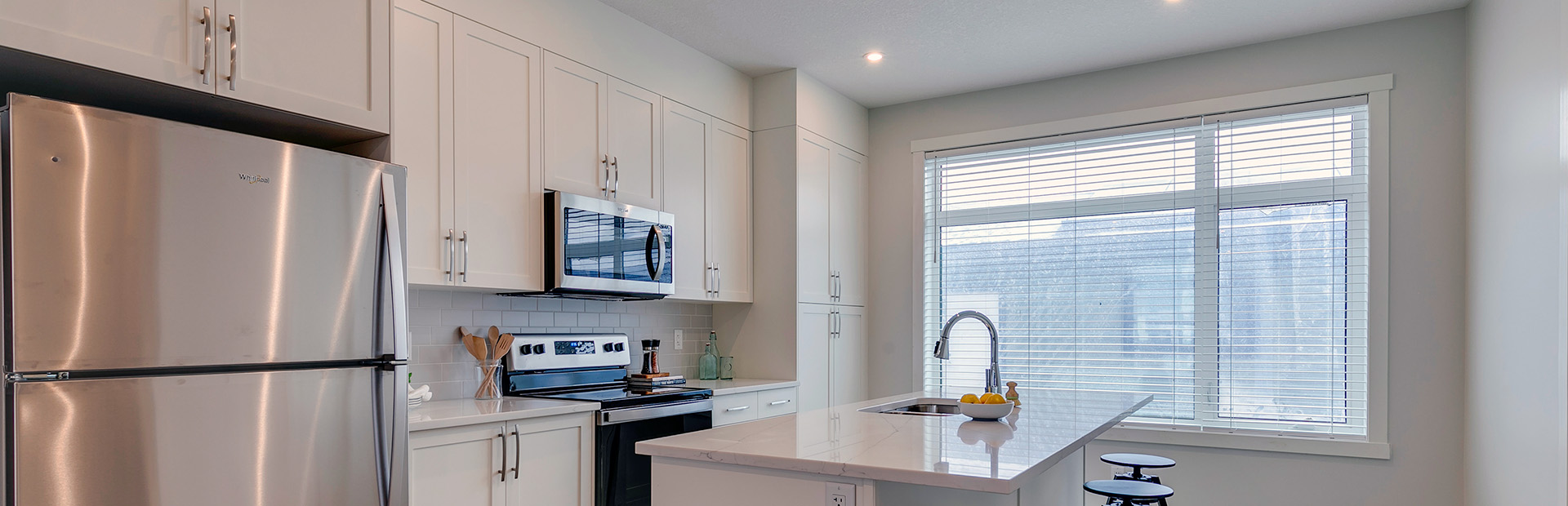 Bright modern kitchen with white cabinetry, stainless steel appliances, and large window providing natural light.