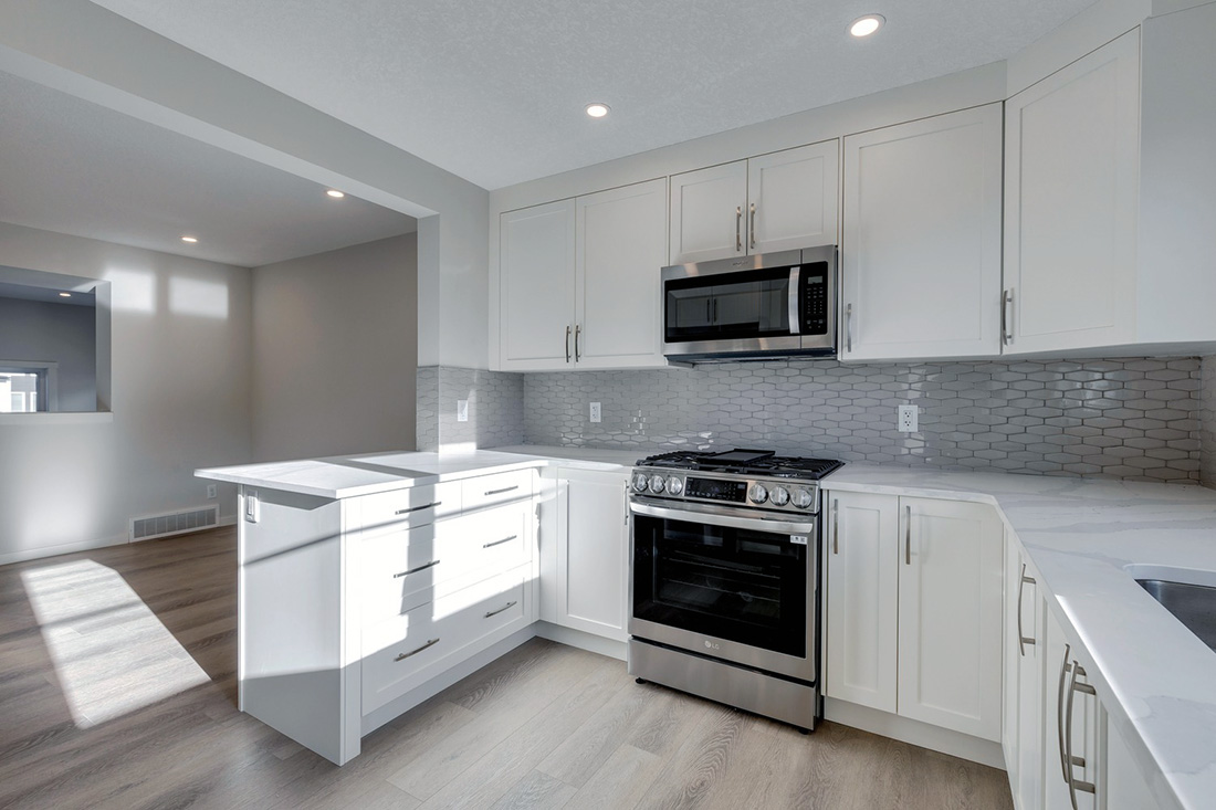 Modern kitchen with white cabinetry, stainless steel appliances, and grey backsplash tile.