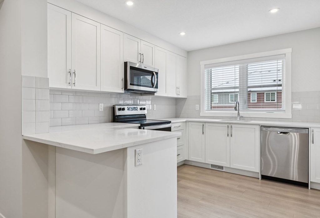 Modern white kitchen with quartz countertops, stainless steel appliances, and a window above the sink