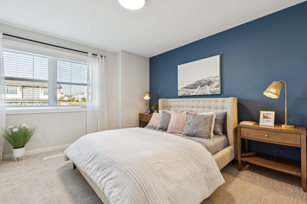 Modern townhouse bedroom featuring a navy blue accent wall, a tufted upholstered bed, and wooden nightstands under a large window with white curtains.