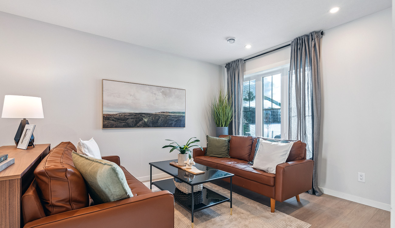 Modern ZEN Livingston living room with brown leather sofas, natural light, and minimalist decor in a Net Zero townhome.