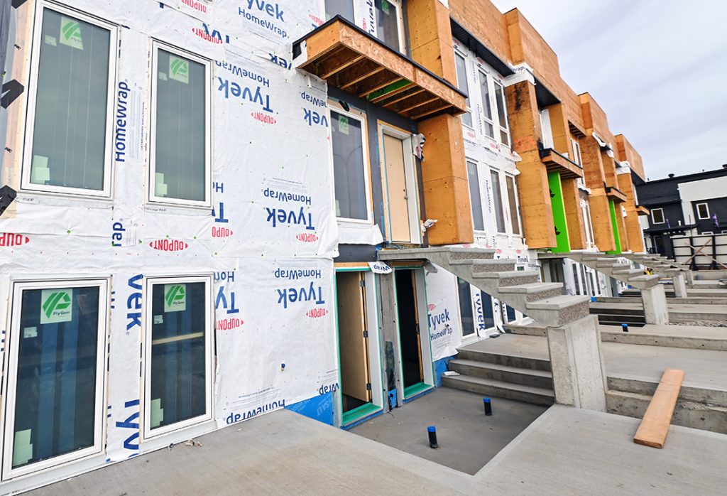 Multi-unit residential townhomes under construction featuring Tyvek house wrap, installed windows, and poured concrete exterior stairs.