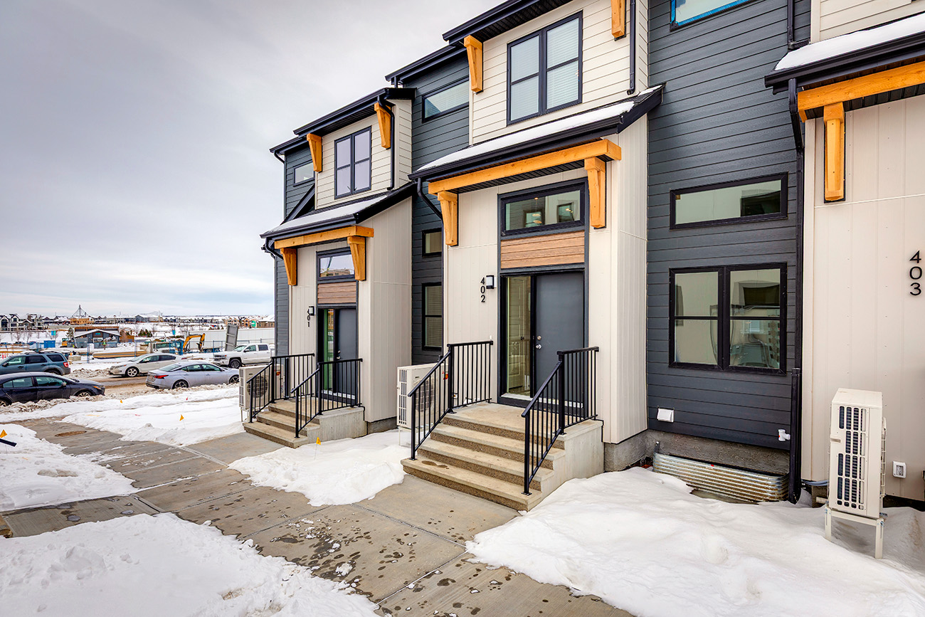 A modern, multi-story townhouse featuring a sophisticated mix of exterior finishes. The facade combines slate-gray horizontal siding with creamy-white vertical panels, accented by light-toned natural wood brackets and trim.