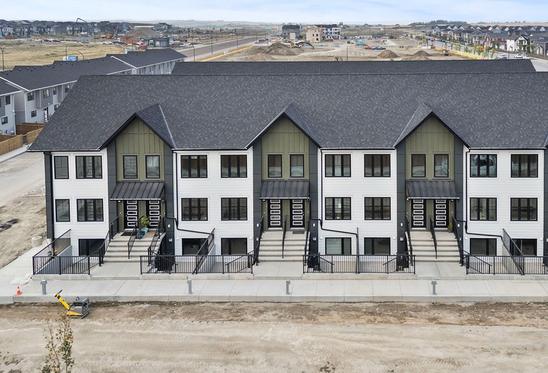 Modern exterior of Zen Livingston townhomes featuring white and olive green siding, black gabled roofs, and metal-awned entryways with black railings.