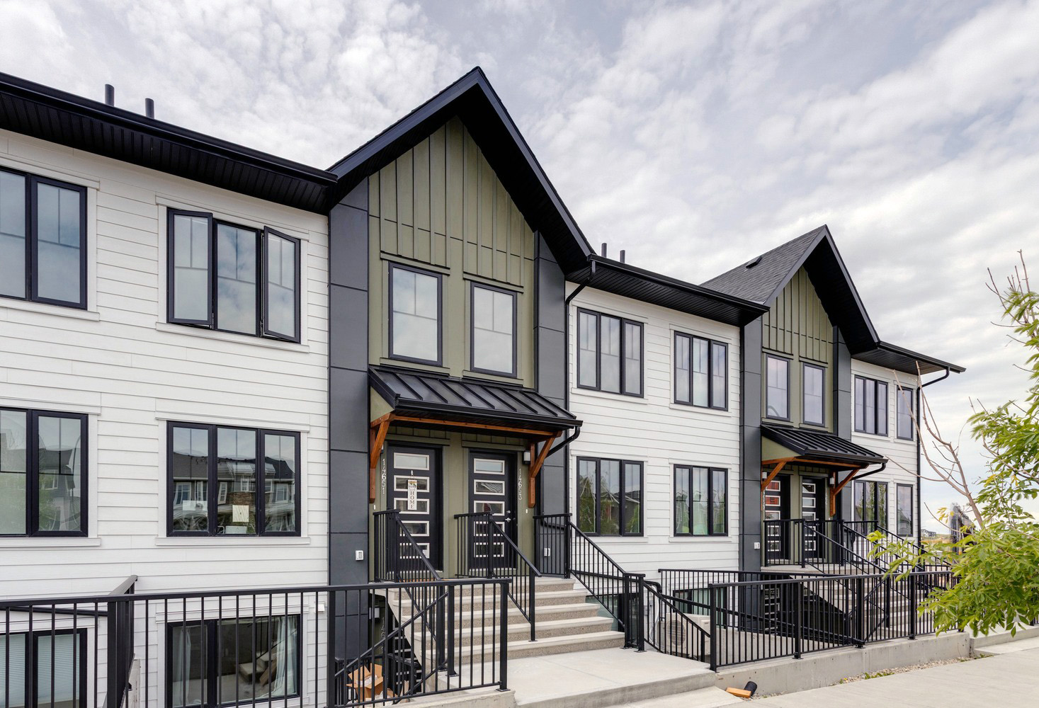Modern exterior of Zen Livingston townhomes featuring white and olive green siding, black gabled roofs, and metal-awned entryways with black railings.